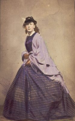 A 19th century photograph, depicting a man in drag. He is posing and wearing mauve attire. Image was found on the "welcome collection" site of the public domain.