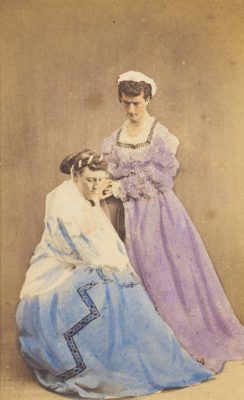 A 19th century photograph, depicting two men in drag. They are posing in the act of dressing. Image was found on the "welcome collection" site of the public domain.