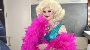 Laura Donorfio in drag attire, wearing a turquoise-colored sequin dress, a large blonde wig, and draped in a hot pink feather boa.